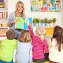 Dzieci w żłobku uczące się liter, siedzące plecami do obiektywu i słuchające pani przedszkolanki.