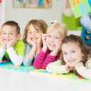 Dzieci w przedszkolu lezące na podłodze, podpierające się rekami i śmiejące się do obiektywu.