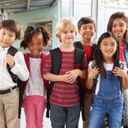 Uśmiechnięte dzieci z tornistrami, stojące na korytarzu w przedszkolu, patrzące do obiektywu.