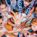 Grupka dzieci w szkole, stojąca w kółku i trzymające się za ręce.