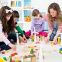 Trójka dzieci w żłobku bawiąca się klockami pod okiem pani przedszkolanki.