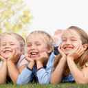 Przedszkolaki leżące na trawie na brzuchu, podpierające się rekami i śmiejące się do siebie.