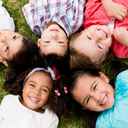 Dzieci leżące w kółku na trawie i uśmiechające się do kamery.